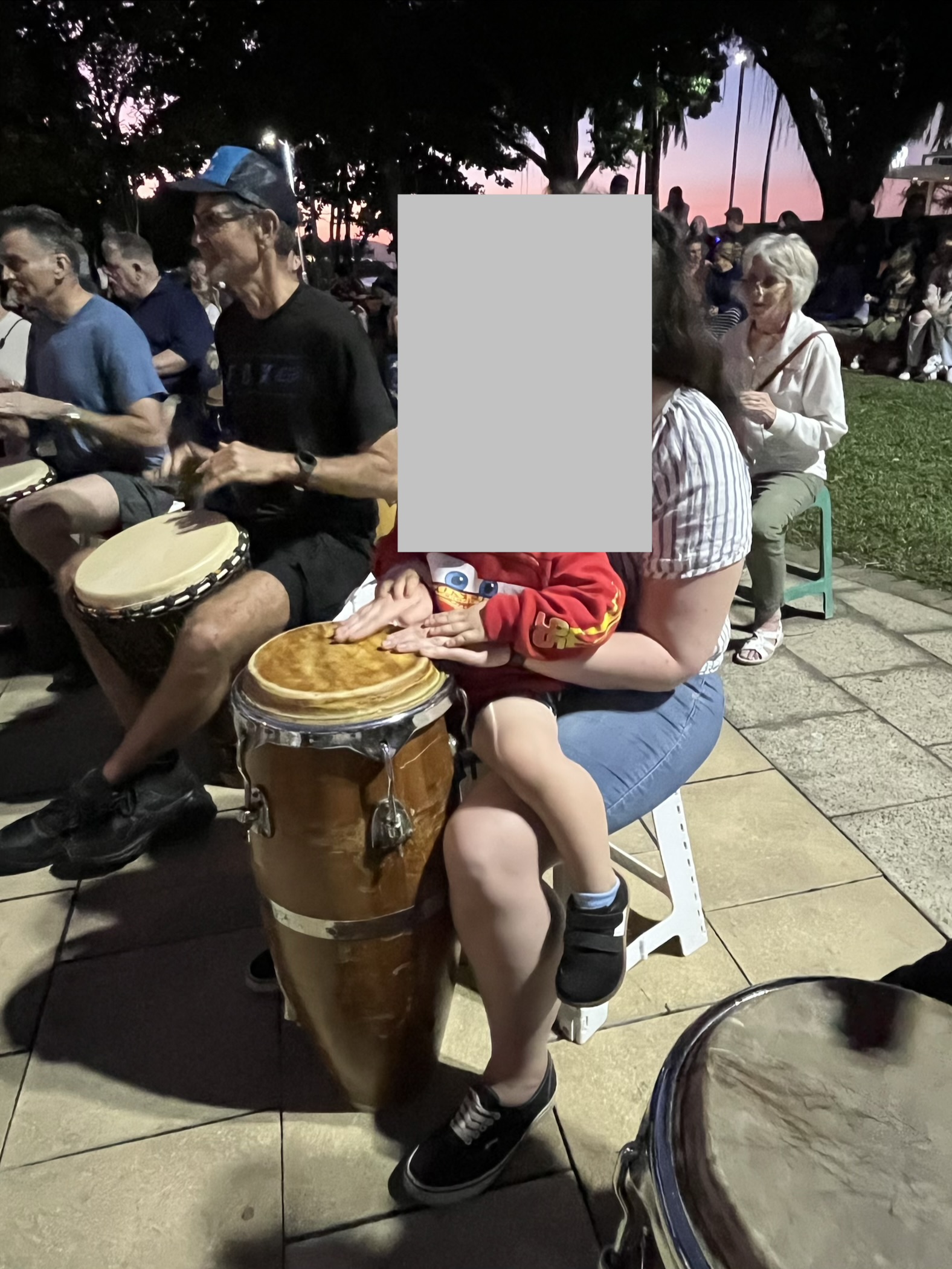 People of different ages playing hand drums together at Townsville's Full Moon Drum Circle on The Strand at dusk