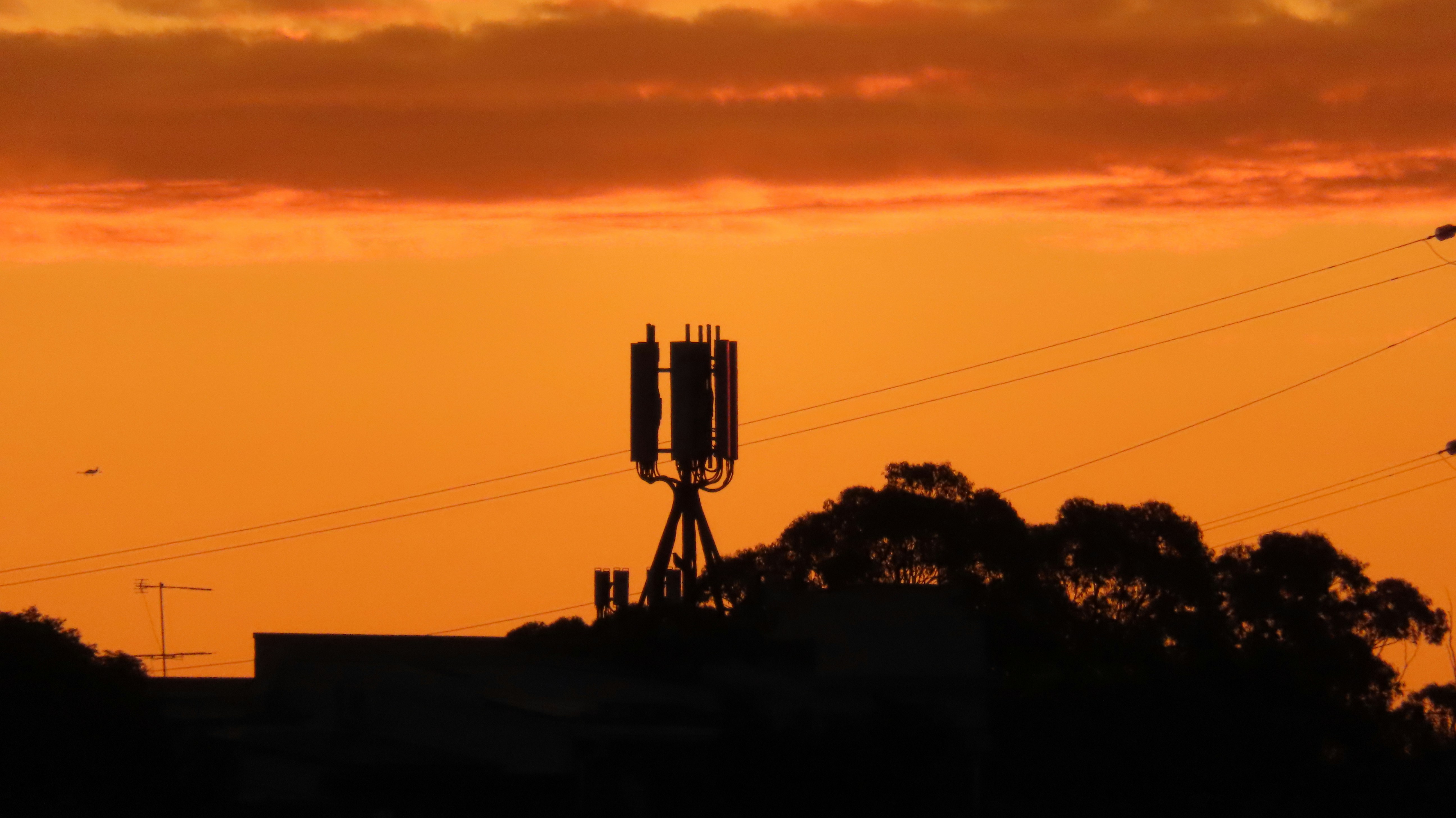 A mobile phone tower silhouetted against an orange sunset