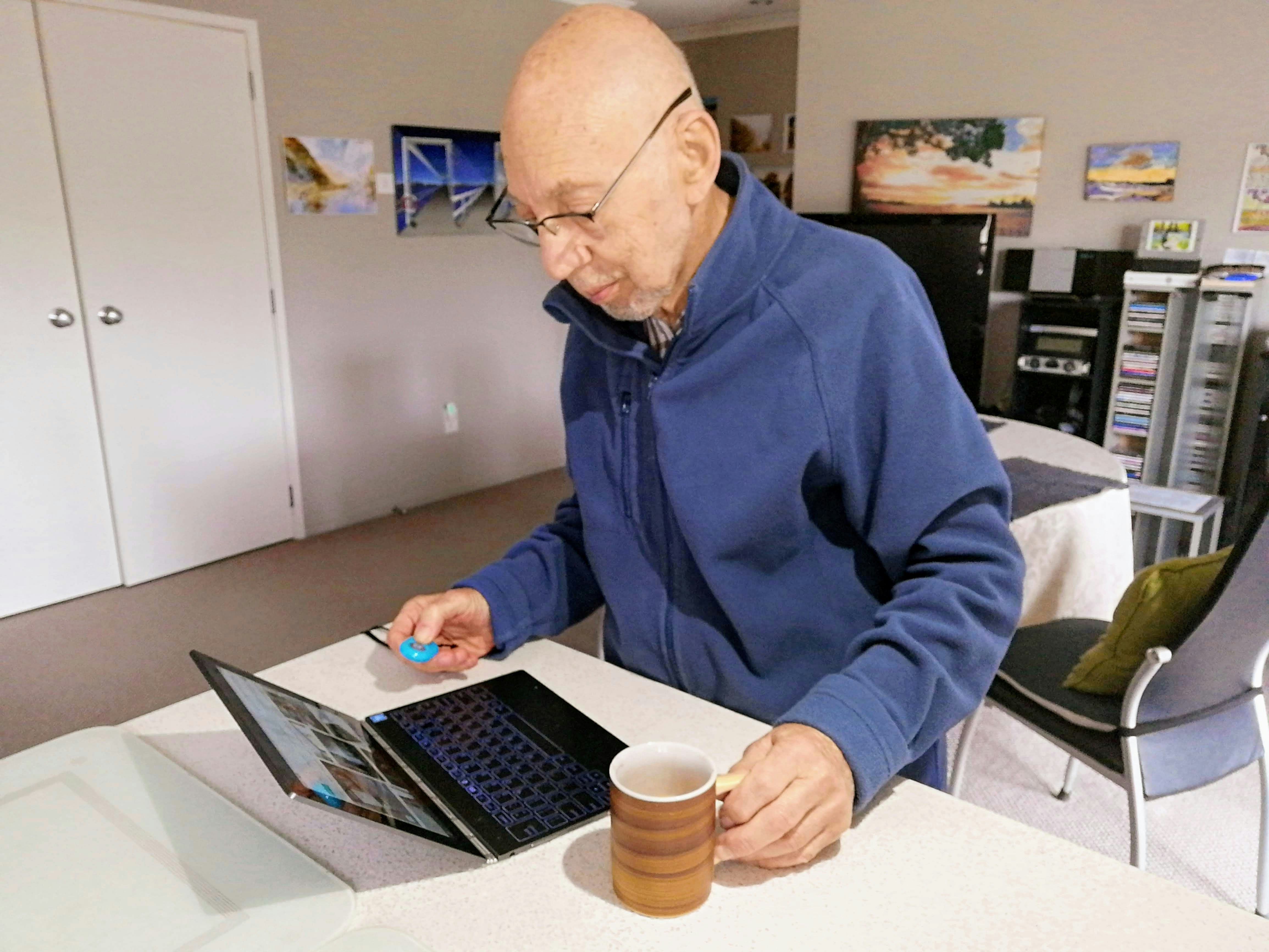 An older man using a laptop at a table with a cup of coffee